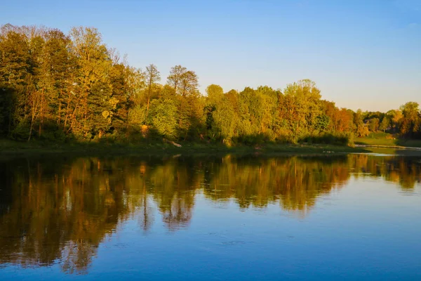 View of a river or lake, reflection of trees in the water, bright rays of the sun fall on the tops of trees, selective focus, nature background.