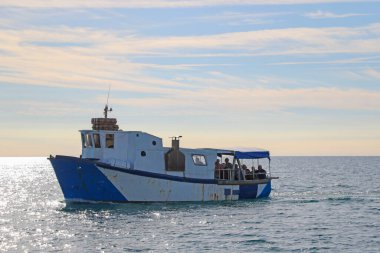 Eski paslı küçük bir tekne insanları taşıyor.