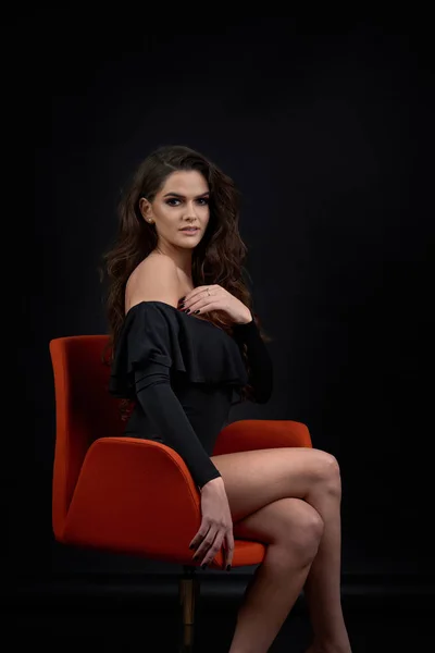 Siyah bir zemin üzerine bir stüdyoda bir kız portresi. Kız kırmızı bir sandalyede oturuyor.
