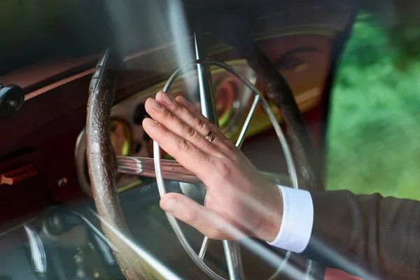 Driver keeps hand on steering wheel of his vintage car.