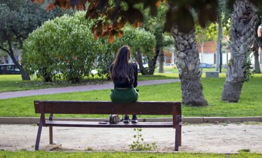 Murcia, İspanya, 15 Nisan 2019: Sonbahar parkında oturan yalnız kadın ya da kız birini bekliyor.