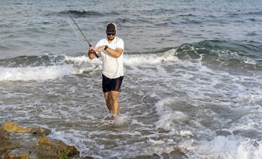 Deniz kıyısında duran balıkçı bir balığı kancaya taktı.