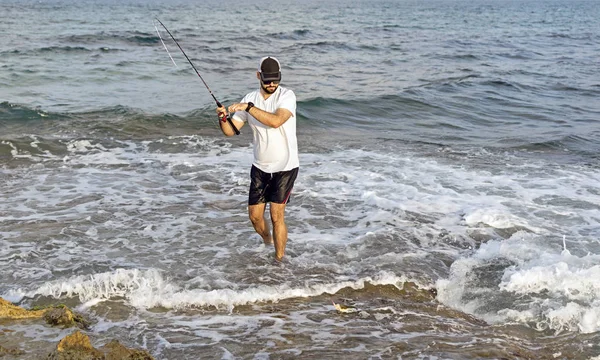 Pescador de pé à beira-mar engancha um peixe . — Fotografia de Stock