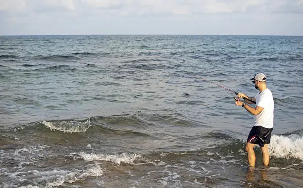 Pescador de pé à beira-mar engancha um peixe . — Fotografia de Stock