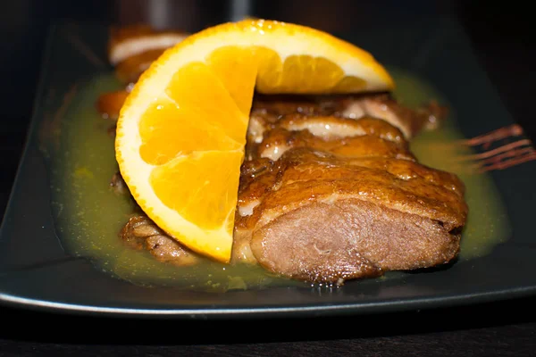 Close-up photo of roasted duck served with orange slices over black background.