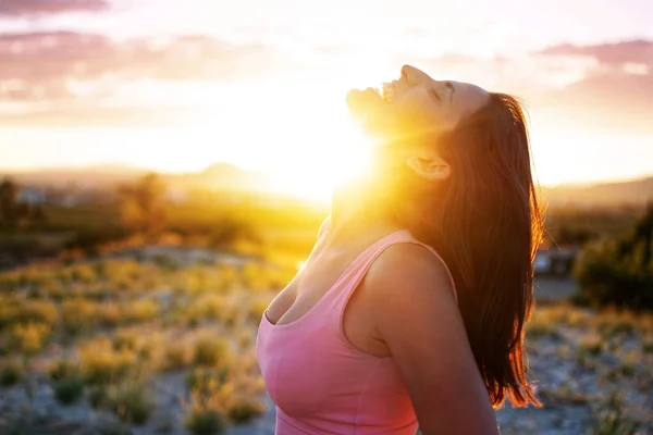 Young girl with open arms freely at mountain top against sunset in Murcia, Spain. Walking and enjoying freedom in countryside. Attractive fit healthy woman in grass field smiling in the air.