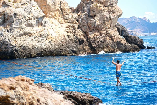 Sportsman keep balance over a slack line. Slackline sport over water. Practice of slack line at mediterranean sea