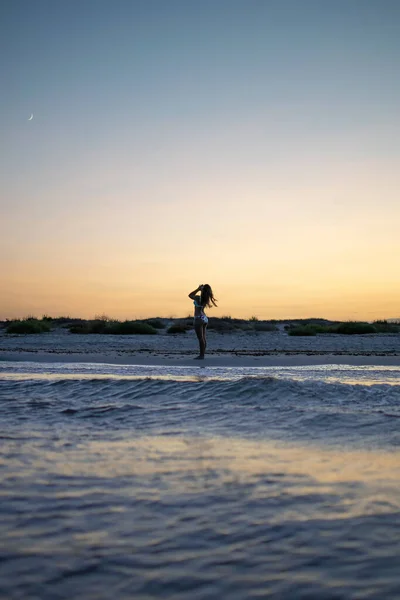 Silhueta jovem mulher de pé na praia ao pôr do sol — Fotografia de Stock