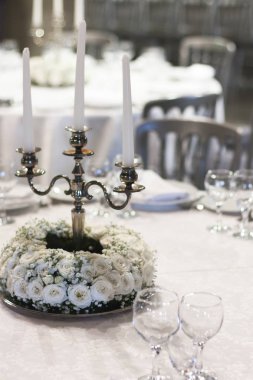 Mumlarla şamdanların etrafında yuvarlak beyaz çiçek dizilimi.