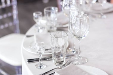 Şarap bardakları masanın üzerinde beyaz bir masa örtüsünün üzerinde. Masa tatil için hazır. Tabaklarda beyaz peçeteler