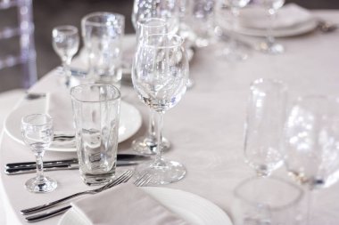 Şarap bardakları masanın üzerinde beyaz bir masa örtüsünün üzerinde. Masa tatil için hazır. Tabaklarda beyaz peçeteler