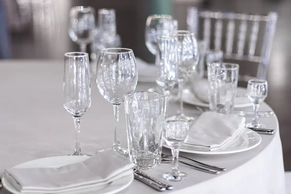 Şarap bardakları masanın üzerinde beyaz bir masa örtüsünün üzerinde. Masa tatil için hazır. Tabaklarda beyaz peçeteler