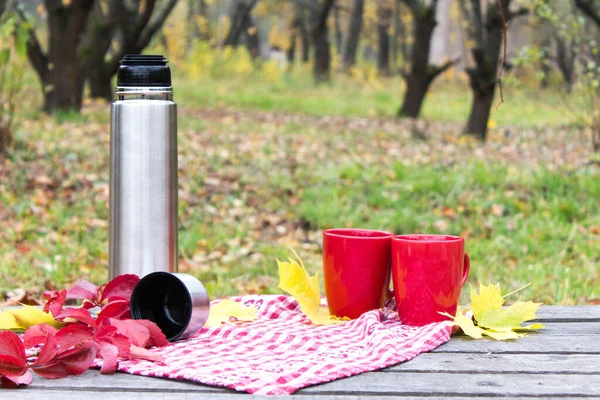秋季野餐，红色的杯子和一个热水瓶放在木制桌子上。秋意盎然 — 图库照片