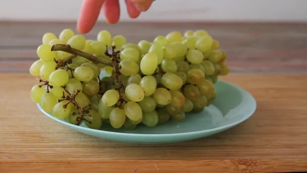 Ženské ruce kladou bílé hrozny na talíř na dřevěný stůl — Stock video