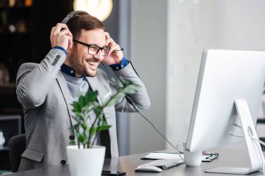 Görüntülü arama yaparken bir bilgisayar ekranına bakarak bir kulaklık ile gülümseyen iş adamı