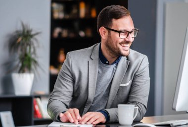 İş yerinde, gözlüklü adam bilgisayar ekranına bakarken gülümseyen