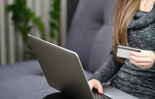 Female person using credit card to pay online on laptop. Sitting on a sofa at home.