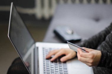 Kadın el kredi kartı için evde, alışveriş online tutarak kanepede oturan