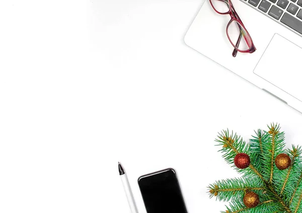 Christmas and new year at the office. White desk top view with laptop, cell phone, glasses and fir branch decoration. Copy space.