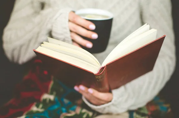 Kadın sıcak içecek sıcak bir yerde tutarak bir kitap okuma