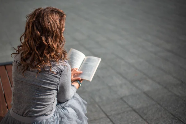 Νέα γυναίκα διαβάζοντας ένα βιβλίο σε ένα παγκάκι, πίσω όψη — Φωτογραφία Αρχείου