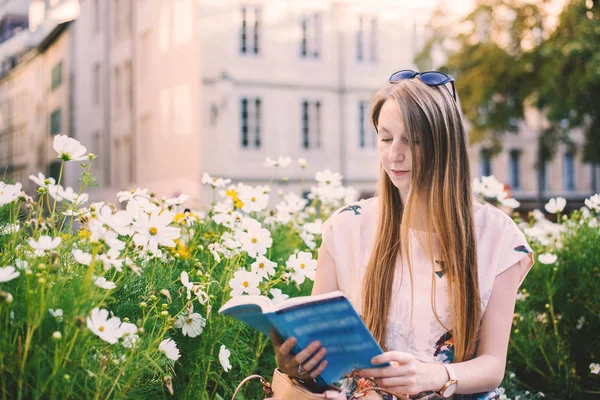 Μακριά μαλλιά γυναίκα κάθεται σε έναν κήπο της πόλης και διαβάζοντας ένα βιβλίο — Φωτογραφία Αρχείου