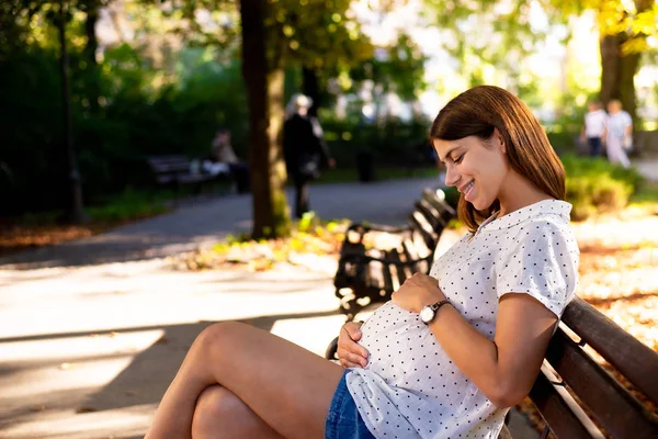 若い妊婦が公園で彼女の腹を優しく保持 — ストック写真