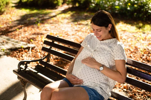 公園に座っている間、彼女の腹を保持している妊娠中の女性 — ストック写真