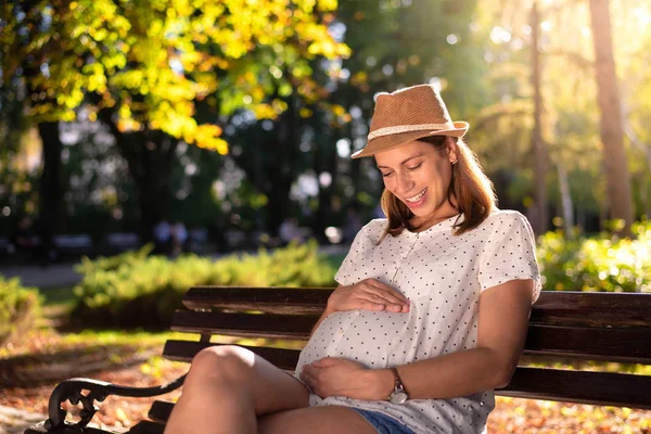 幸せな若い妊娠中の母親は彼女の大きな鐘を見ながら微笑む — ストック写真