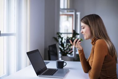 Telefondaki ses tanıma sistemini kullanan genç bir ofis çalışanı.