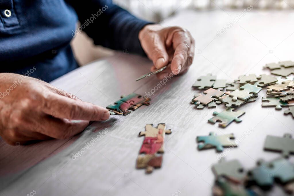 Senior person connecting jigsaw puzzles, closeup of the wrinkled hands. Stay home concept. 