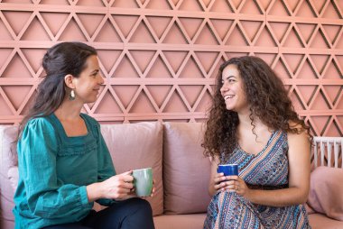 İki güzel, gülümseyen bayan arkadaş çay ya da kahve içerken, pembe bir kanepede otururken güzel bir sohbet ediyorlar.. 