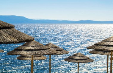 Deniz kenarı tatil sahnesi - güneşli bir yaz gününde mavi güneşli deniz ve parlak şemsiyeler.