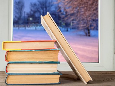 books on the desk against the window with a winter landscape at sunrise clipart