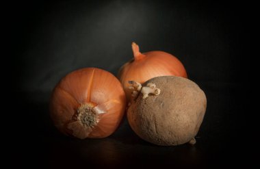 patates ve yüzey üzerinde siyah bir zemin üzerine iki soğan