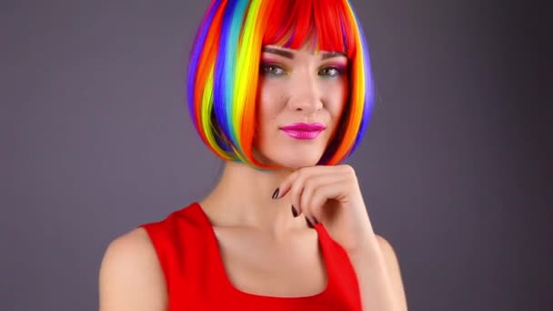 穿着彩虹色假发和红色礼服的年轻女子站在灰色背景上 — 图库视频影像