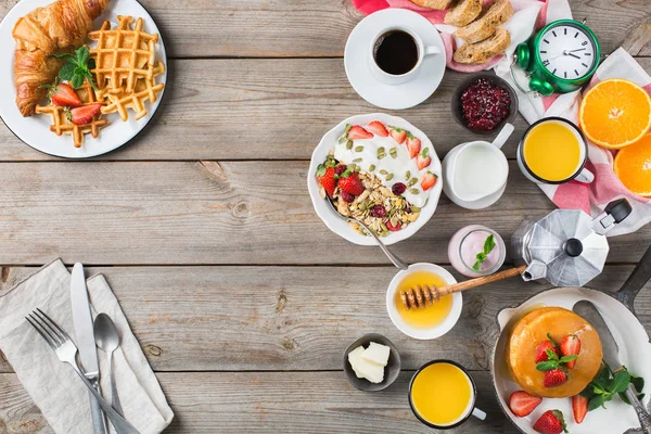 Food and drink, healthy morning eating concept. Breakfast assortment with pancakes, waffles, croissant sandwich and granola with yogurt on the wooden table. Top view flat lay background