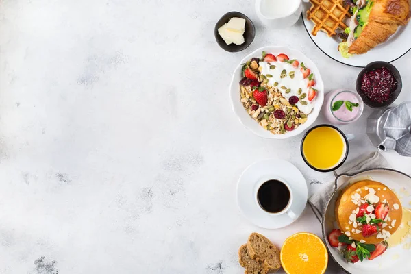 Food and drink, healthy morning eating concept. Breakfast assortment with pancakes, waffles, croissant sandwich and granola with yogurt on the kitchen table. Top view flat lay copy space background