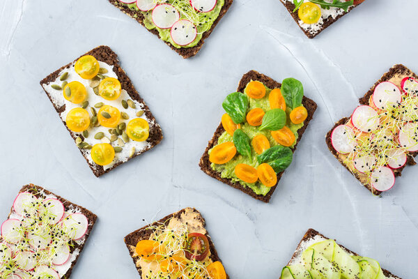 Food and drink, still life concept. Variety of handmade sandwiches with cream cheese, hummus, avocado, vegetables and micro greens sprouts for lunch table. Top view flat lay background