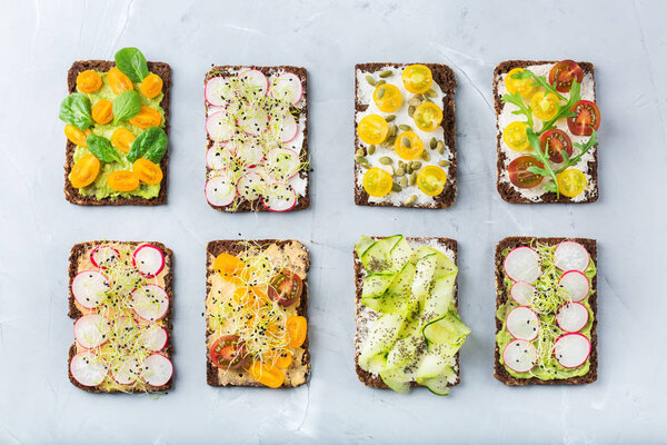 Food and drink, still life concept. Variety of handmade sandwiches with cream cheese, hummus, avocado, vegetables and micro greens sprouts for lunch table. Top view flat lay background