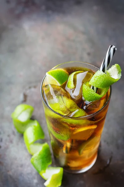 Food and drink, holidays party concept. Alcohol cocktail with rum and cola cuba libre beverage, longdrink in a glass with straw, ice and lime zest on a dark table