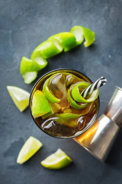 Food and drink, holidays party concept. Alcohol cocktail with rum and cola cuba libre beverage, longdrink in a glass with straw, ice and lime zest on a dark table. Top view background