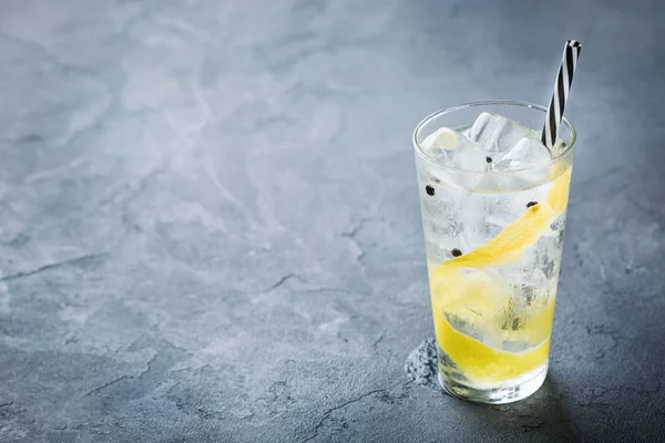 Food and drink, holidays party concept. Gin and tonic alcohol cocktail drink with ice and lemon zest in a glass on a grunge dark table. Copy space background