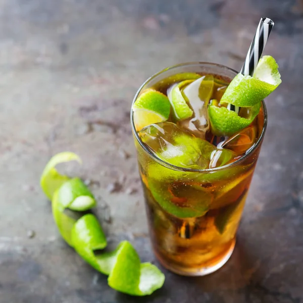 Food and drink, holidays party concept. Alcohol cocktail with rum and cola cuba libre beverage, longdrink in a glass with straw, ice and lime zest on a dark table