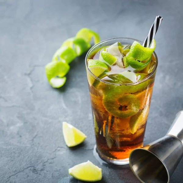 Food and drink, holidays party concept. Alcohol cocktail with rum and cola cuba libre beverage, longdrink in a glass with straw, ice and lime zest on a dark table