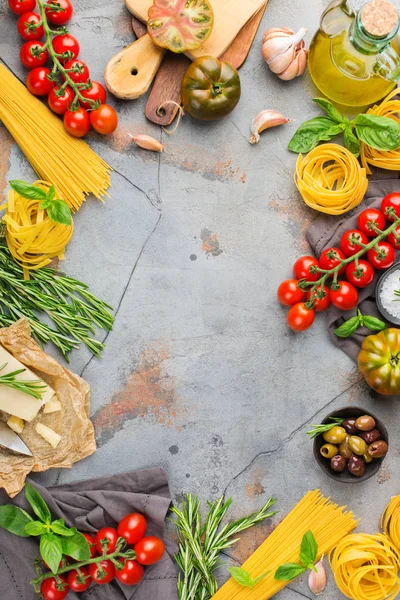 Italian food ingredients cooking background with pasta, olive oil, parmesan cheese, green basil, ripe tomatoes, garlic, herbs. Copy space flat lay top view background