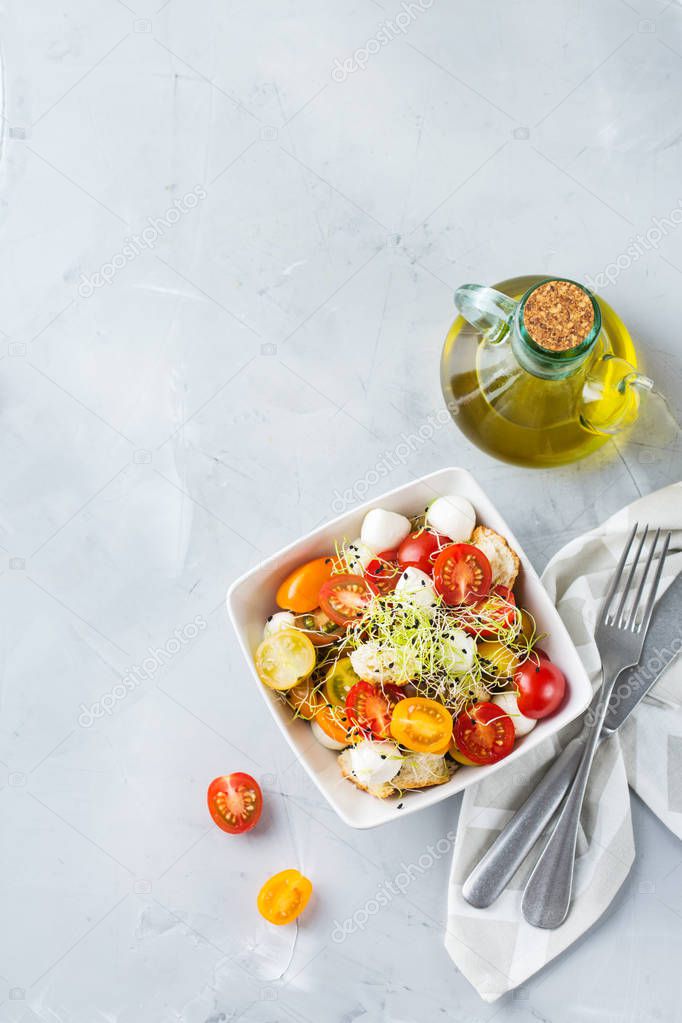 Food and drink, healthy eating concept. Salad with assortment of organic cherry tomatoes, mozzarella cheese, toasted bread and microgreen on a kitchen table. Top view flat lay background