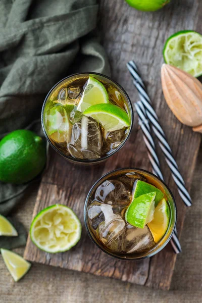 Food and drink, holidays party concept. Cuba libre or long island iced tea alcohol cocktail drink beverage, longdrink in a glass with straw, ice and lime on a dark table. Top view flat lay