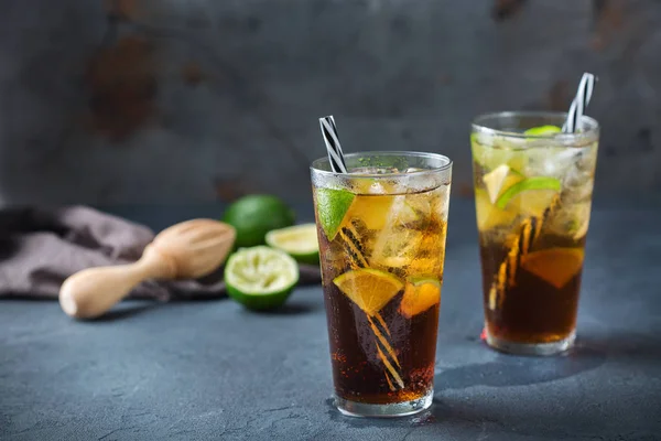 Food and drink, holidays party concept. Cuba libre or long island iced tea alcohol cocktail drink beverage, longdrink in a glass with straw, ice and lime on a dark table