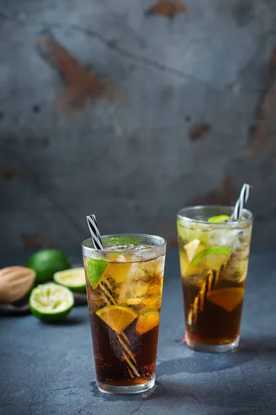 Food and drink, holidays party concept. Cuba libre or long island iced tea alcohol cocktail drink beverage, longdrink in a glass with straw, ice and lime on a dark table